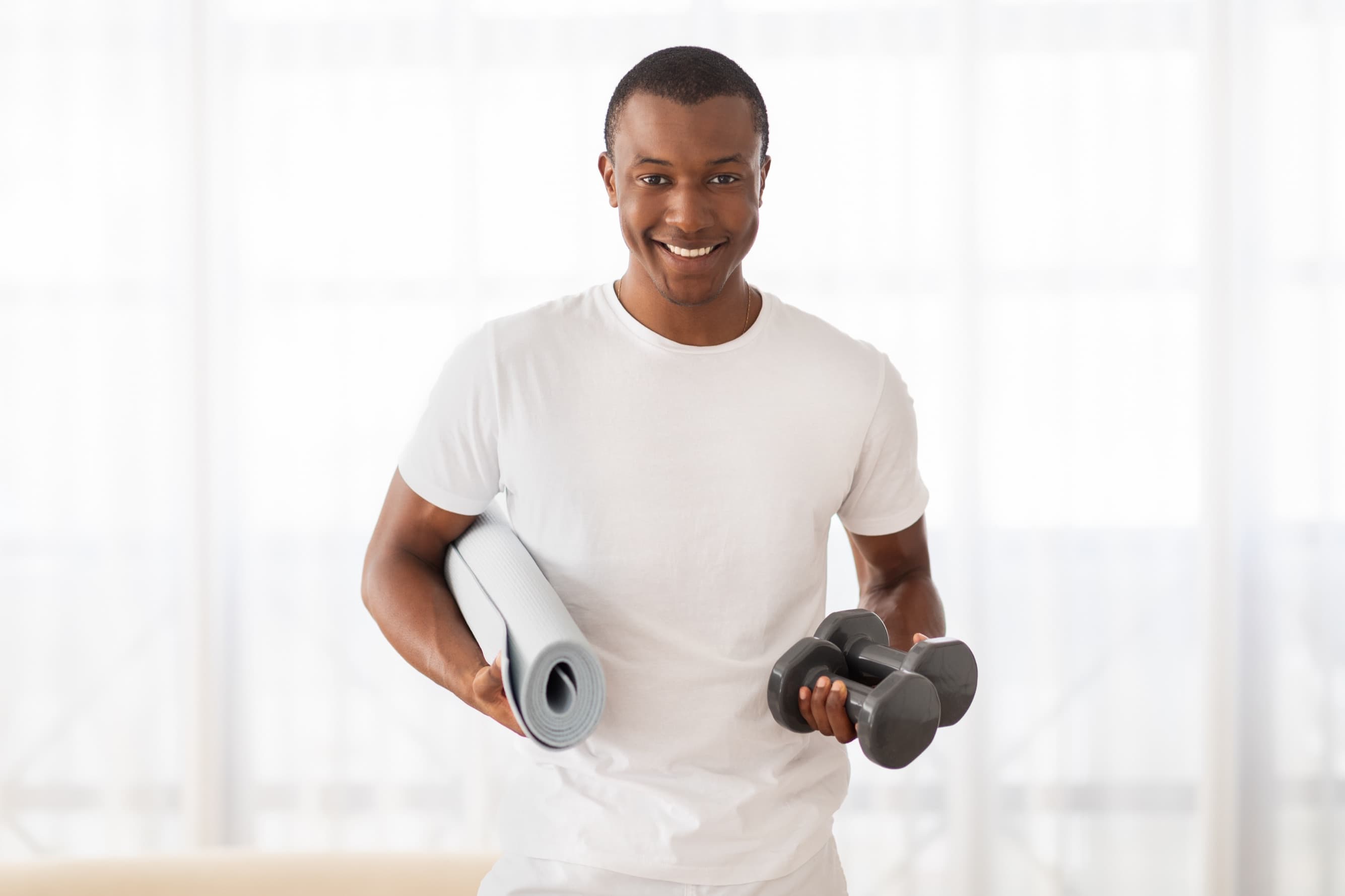 Black fitness and wellness trainer holding a yoga mat and dumbbells